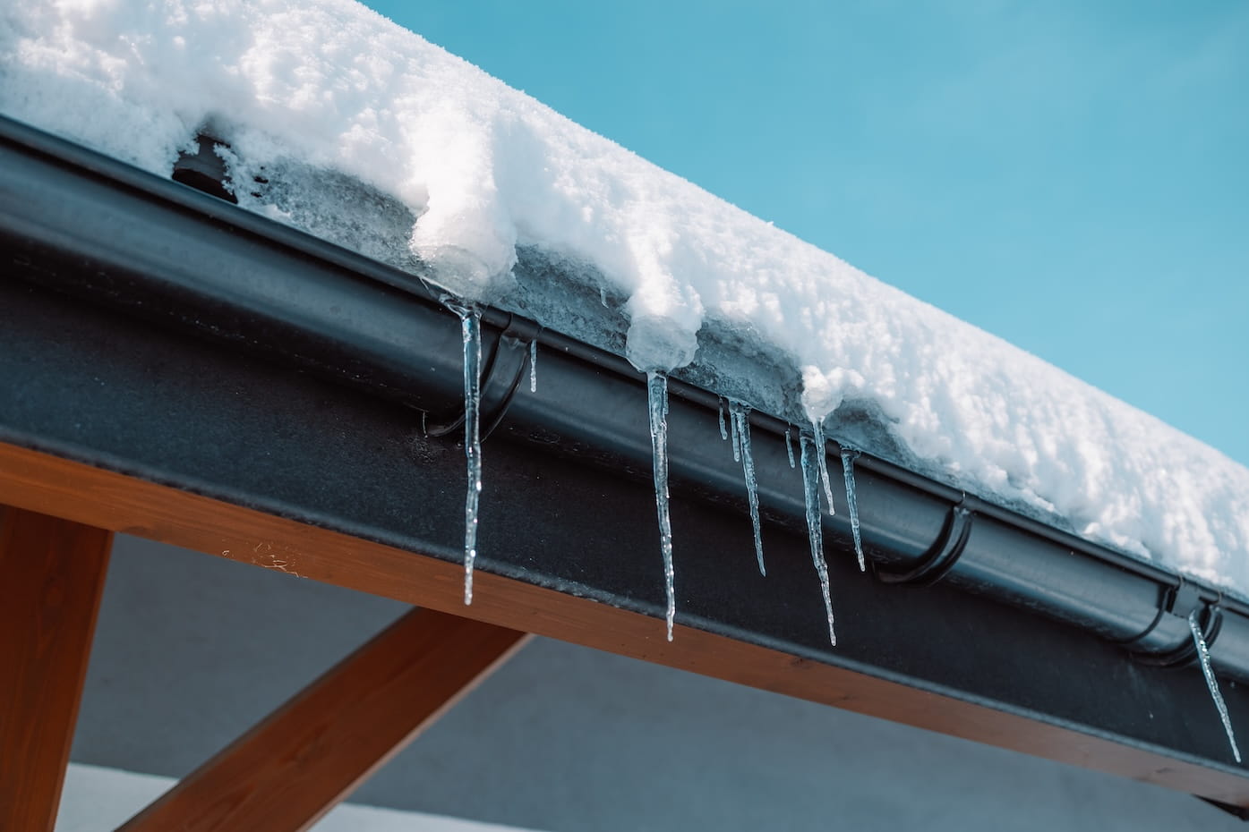 Icicles hang from the roof of a log house near which a car is carelessly parked, which can be damaged by falling ice floes.